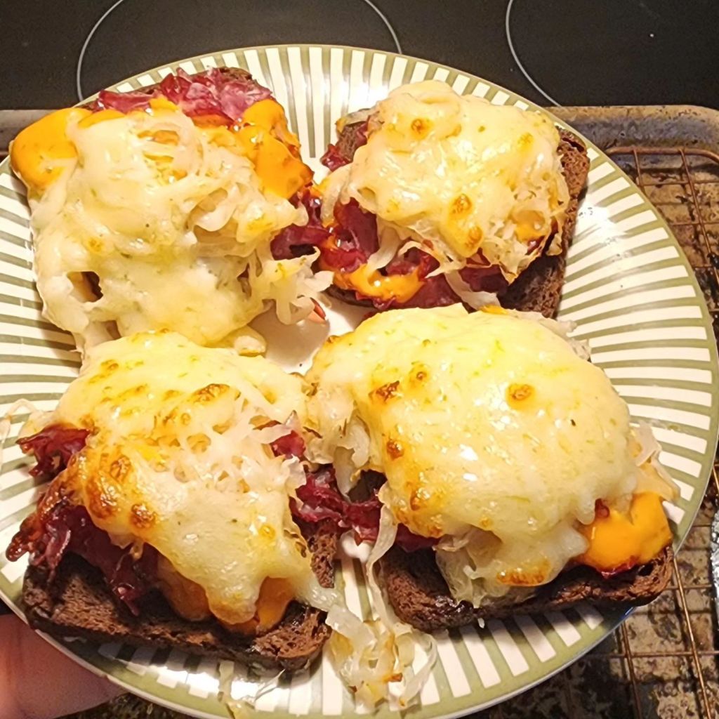 Four Reuben cocktail pumpernickel bread appetizers arranged on a plate.