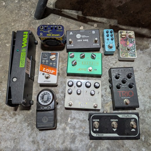 A bunch of guitar  pedals on the dirty concrete floor.