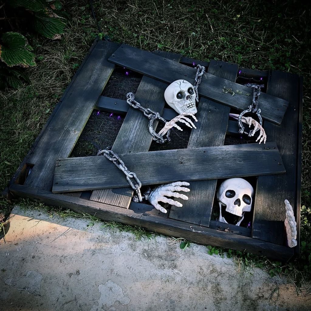 Halloween decoration featuring skeletons appearing to escape from a wooden dungeon, complete with chains and hands reaching out.