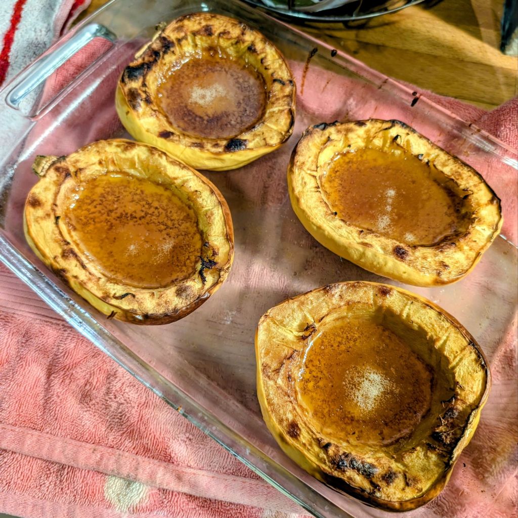Baked acorn squash halves caramelized and arranged in a glass dish, featuring a slightly charred edge and a sweet, golden center.