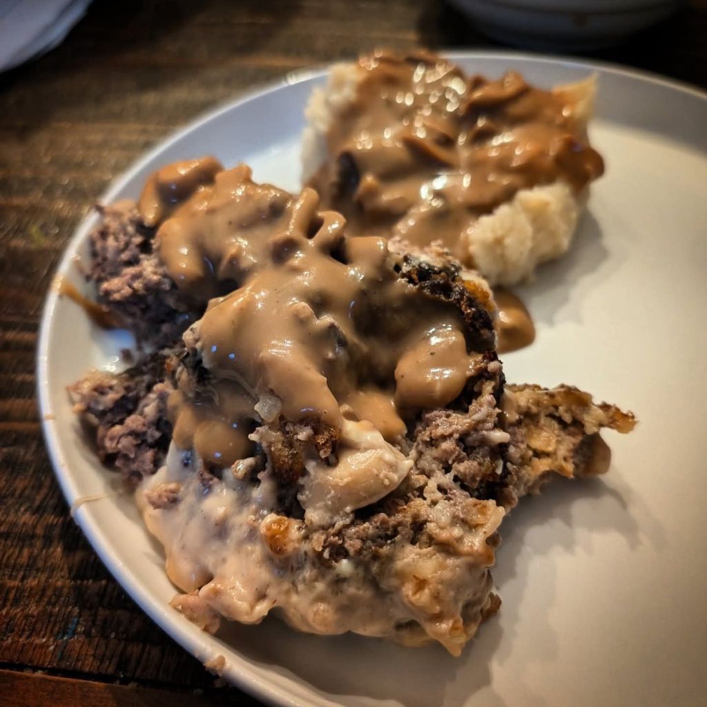 A serving of meatloaf topped with gravy, accompanied by a side of mashed potatoes on a white plate.