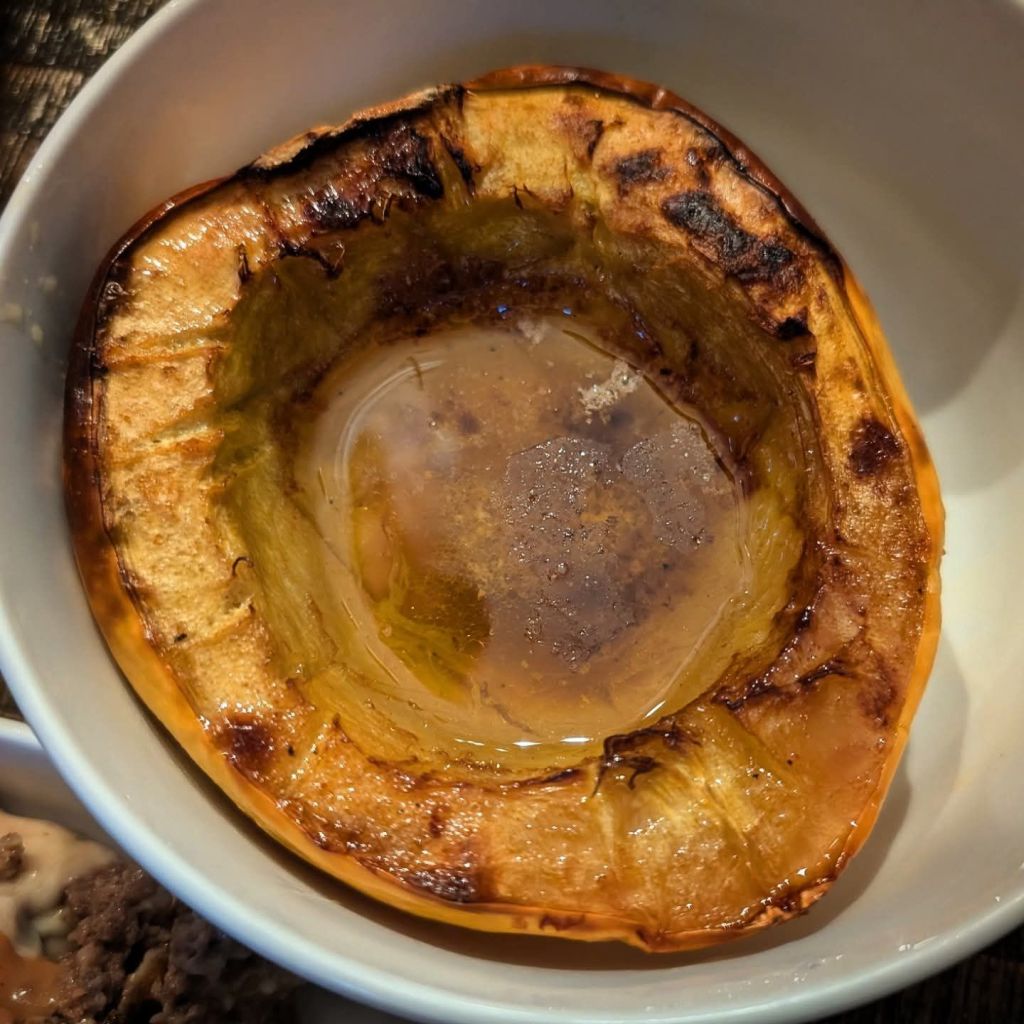A bowl containing roasted acorn squash, with a golden-brown exterior and a small pool of liquid inside.