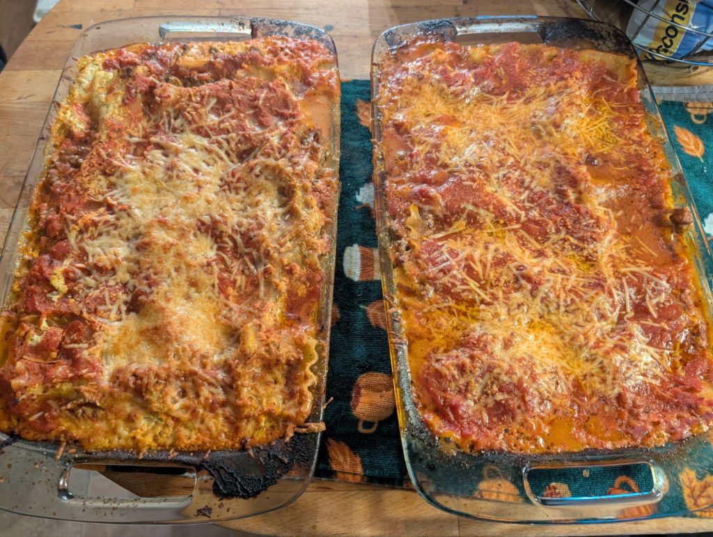 Two glass baking dishes filled with baked lasagna, topped with melted cheese and marinara sauce, resting on a wooden surface.
