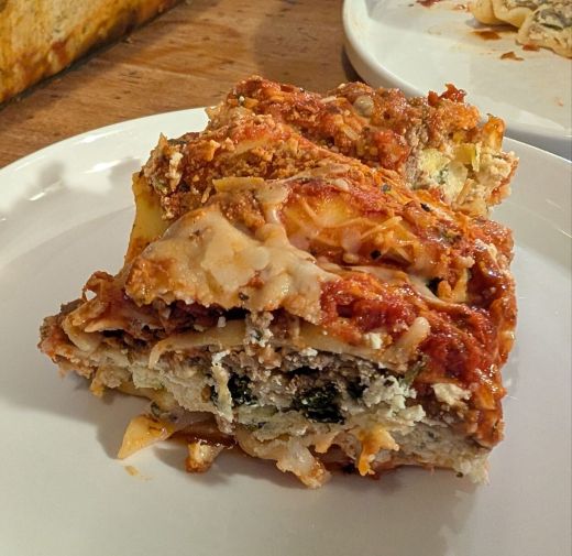A slice of lasagna on a white plate, showcasing layers of pasta, ricotta cheese, meat, and marinara sauce.