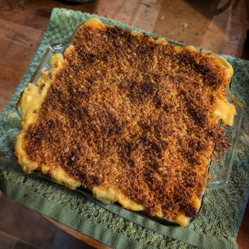 A baked mac and cheese dish with a golden brown breadcrumb topping, placed on a green towel.