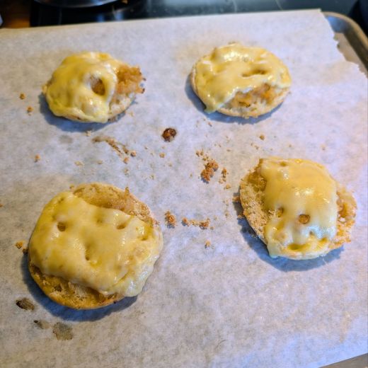 Four toasted English muffin halves topped with caramelized onions & melted Swiss cheese on a baking sheet lined with parchment paper.