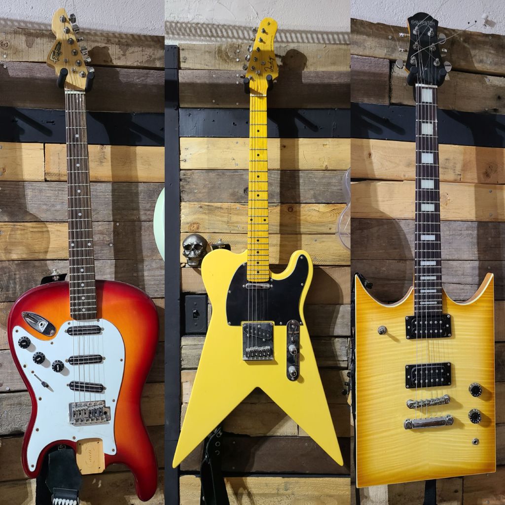 Dewey Decibel FlipOut: A vintage-style sunburst electric guitar featuring an inverted S-style body shape, a white multi-pickup guard equipped with three single-coil pickups, a standard tremolo bridge, control knobs clustered on the lower horn, and a maple neck with a dark fretboard and distinctive headstock shape.
Indy Custom FlyCaster: A bright yellow electric guitar with a custom modified shape combining T-style elements and sharp V-style bottom points, featuring a solid yellow finish, a black pickguard, two single-coil pickups, a standard bridge, and a matching yellow maple neck and fretboard with a pointed headstock.
Galveston B.B. Stone: A honey-burst, flamed-top electric guitar boasting an aggressive, angular dual-cutaway body shape, a bound fretboard with large block inlays, dual black humbucker pickups, a Tune-o-matic style bridge with a stopbar tailpiece, control knobs placed along the lower right edge, and a dark headstock bearing the Galveston logo.