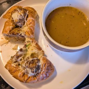 A toasted wedding-soup inspired meatball sub cut in half on a plate, served alongside a warm bowl of flavorful golden brodo di bollito.