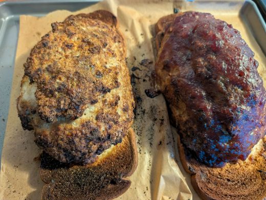 A poorly composed photo of two turkey meatloaves fresh from the oven, sitting on toasted bread slices on a parchment-lined baking sheet. The one on the left plain with golden-brown evidence of the Maillard reaction, the one on the right topped with a glistening deep red cranberry glaze. This was obviously taken by a hangry man in a hurry to eat.