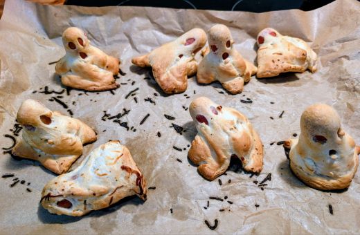 8 hot dog ghosts in various positions after baking on top of parchment paper on a baking sheet.