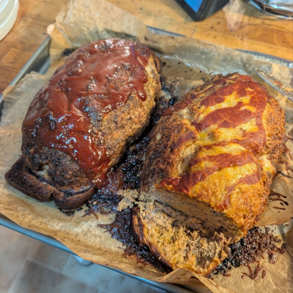 A "normal" meatloaf and a Taco Night Meatloaf side by side on a parchment lined baking sheet.
