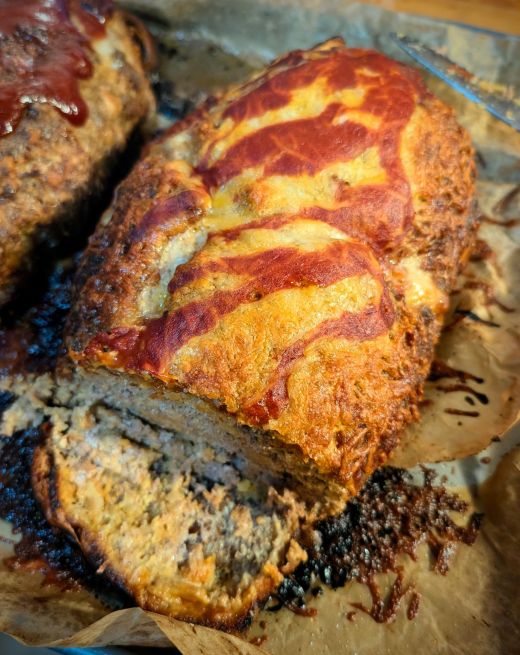 A taco-inspired meatloaf topped with melted cheese and taco sauce atop of a parchment lined baking sheet.